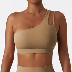 A tan, one-shoulder sports bra with a thin strap detail on the left side.