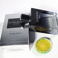 A bottle of 100ML OEM/ODM EDP men perfume long lasting fragrance and perfume sits on its silver box with a lime slice-shaped object close by on a white surface.