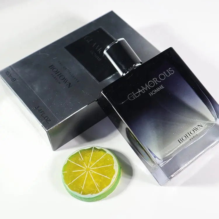 A 100ML OEM/ODM EDP men's perfume with long-lasting fragrance rests beside its box, accented by a decorative lime slice on a white surface.