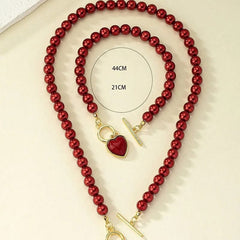 A jewelry set featuring a red imitation pearl necklace and bracelet with a gold heart pendant.