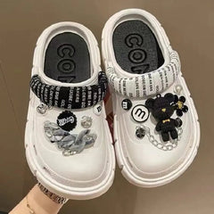 A pair of white platform clogs for women decorated with various black and silver charms.