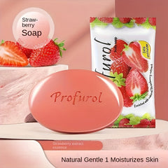 A pink oval strawberry scented soap bar is displayed next to its strawberry-themed packaging.