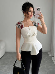 A woman wears a white sleeveless square neck blouse with floral mesh shoulders and an asymmetrical hem.