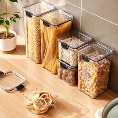 A set of five clear, rectangular plastic storage containers with black locking lids on a counter.