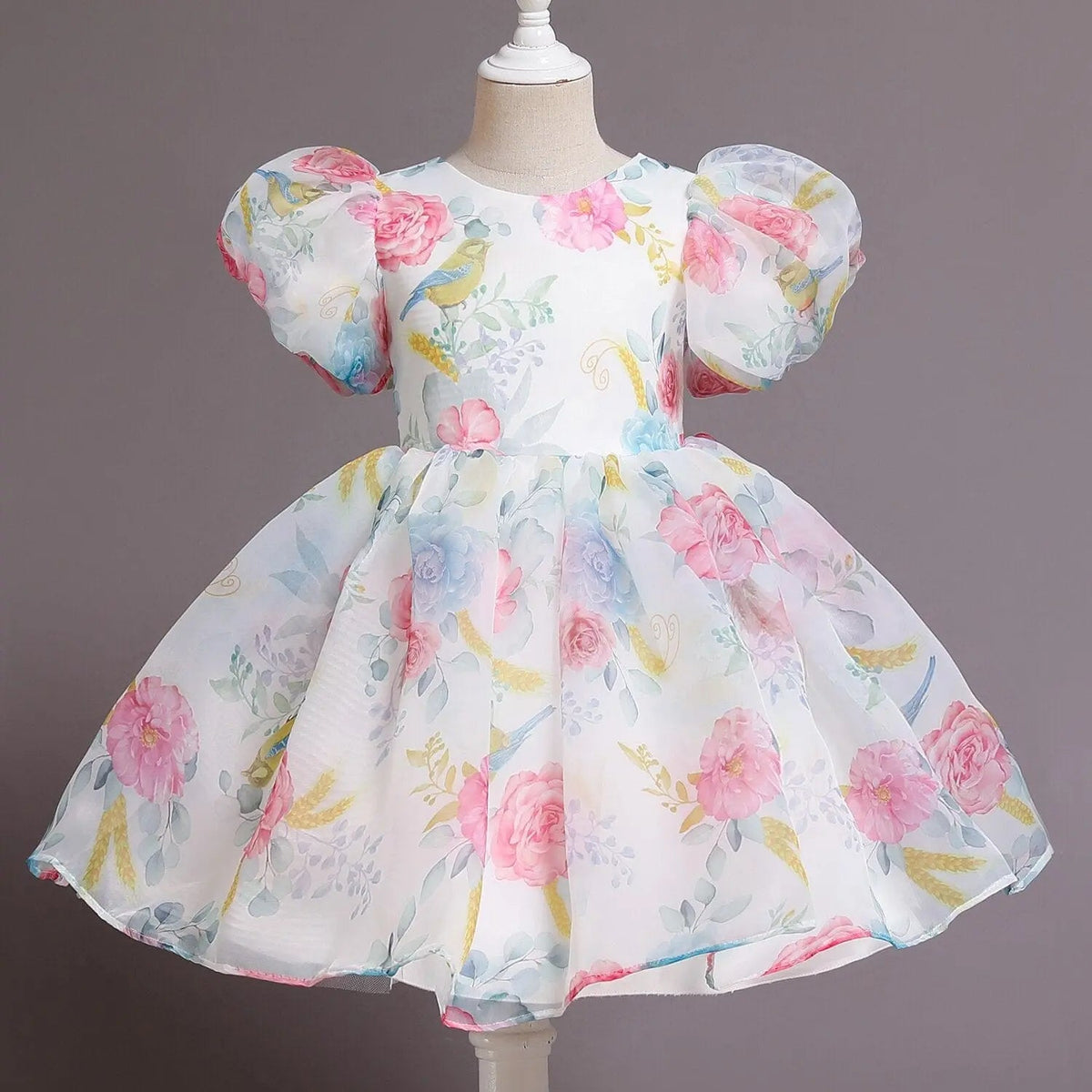 A white girl's ball gown dress featuring a floral print, puff sleeves, and a full skirt.