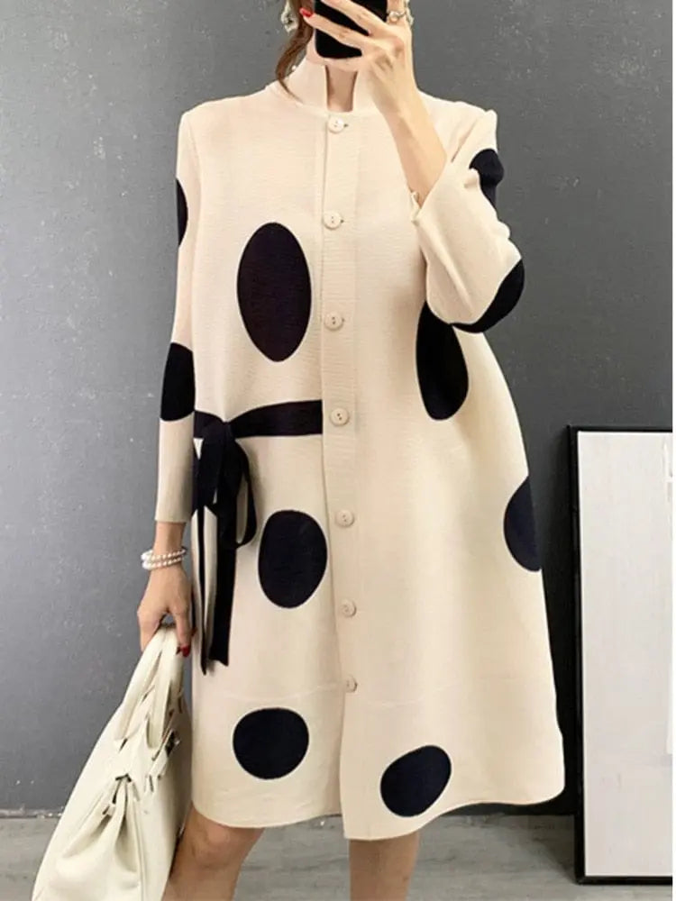 A person wears the Elegant Stand Collar Pleated Dress, featuring a cream base with large black polka dots, button-down front, and black waist bow, paired with a white handbag.