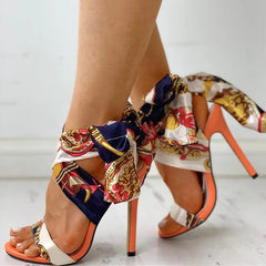 A pair of open-toe stiletto heels featuring a colorful patterned silk ribbon ankle tie.