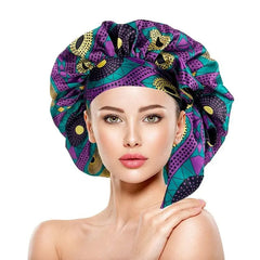 A woman wears an extra-large satin bonnet featuring a vibrant purple and teal African print pattern.