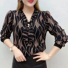 A woman wears a black V-neck blouse with a wavy pattern and a decorative pearl-accented tie.