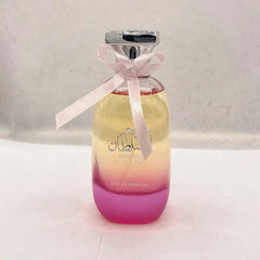 A bottle of Hareem Al Sultan perfume with a pink bow and a pink to yellow gradient glass base.