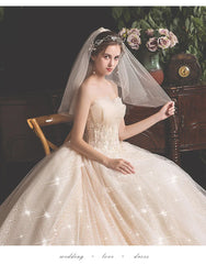 A woman wears a strapless champagne-colored wedding dress with lace detailing and a veil.