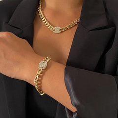 A person in a black blazer showcases the Ingemark Iced Out Rhinestones Tennis Chain Choker Necklace featuring a round CZ-studded clasp, paired with a matching bracelet.