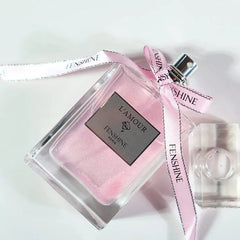 A square glass bottle of Fenshine L'Amour perfume with pink liquid and a branded ribbon.