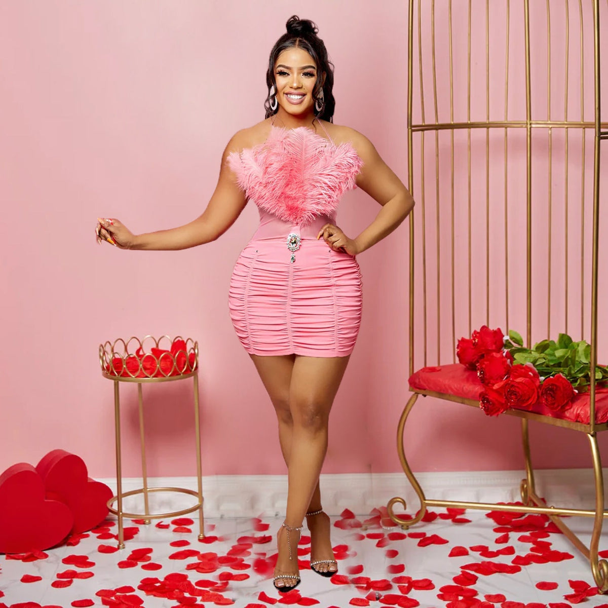 A woman wears a pink sleeveless tube top dress featuring a feathered bodice and ruched skirt.