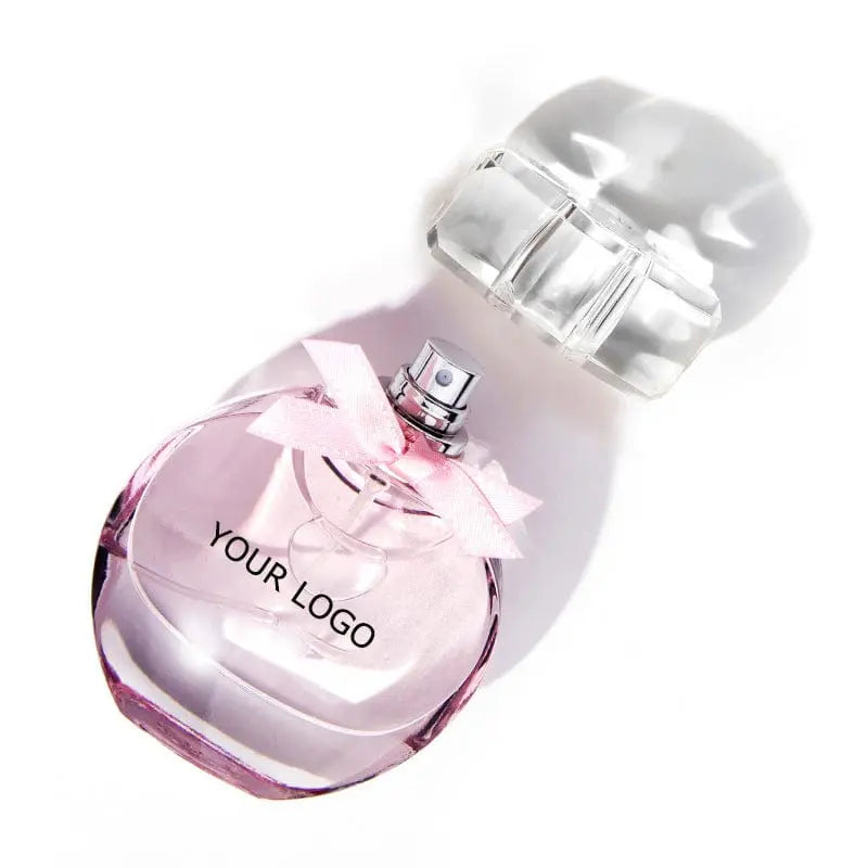 The Perfume Customize Luxury Fragrance OEM Perfume features pink liquid in a clear glass bottle with a light pink ribbon and cap beside it, showcasing an elegant, feminine look—perfect for private label luxury and long-lasting EDP.