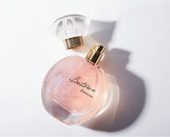A round glass perfume bottle with shimmering pink liquid and a detached clear cap.