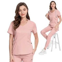 A woman wearing a pink V-neck scrub top and matching jogger pants.