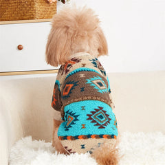 A small dog wears a khaki, brown, and turquoise fleece sweater with a geometric totem print.