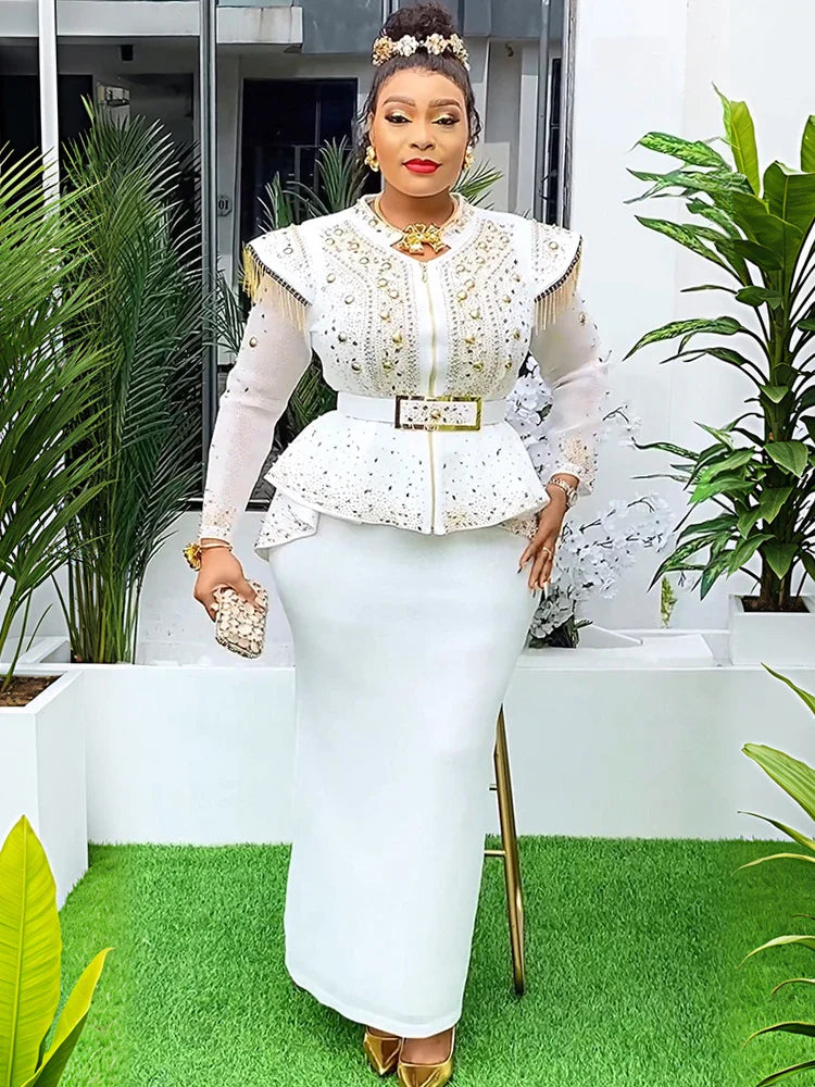 A woman wears a white two-piece set featuring a beaded peplum top with gold accents and a skirt.
