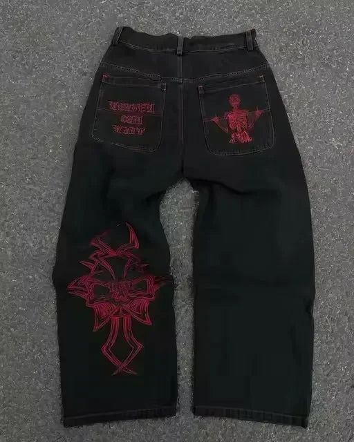 Blue low-rise flared denim jeans with rhinestone wing embroidery, studded pockets, and streetwear style from American Vintage Y2K collection.