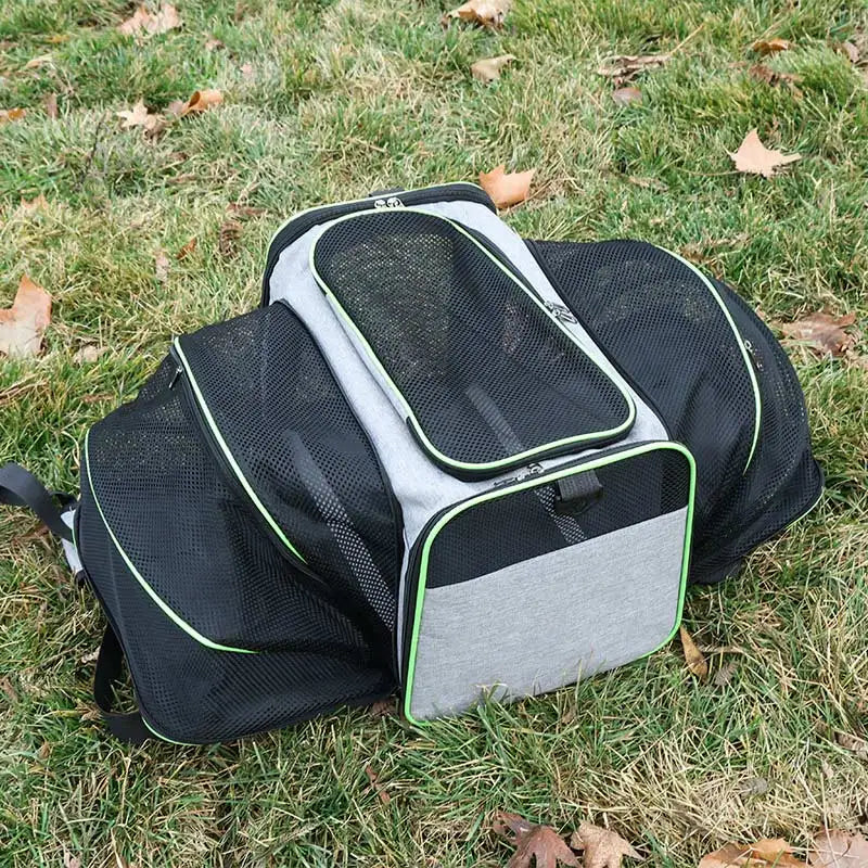 A grey and black expandable pet carrier with mesh panels sitting on grass.