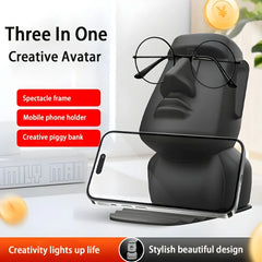 A black Moai statue desk accessory that functions as a glasses holder, phone stand, and piggy bank.