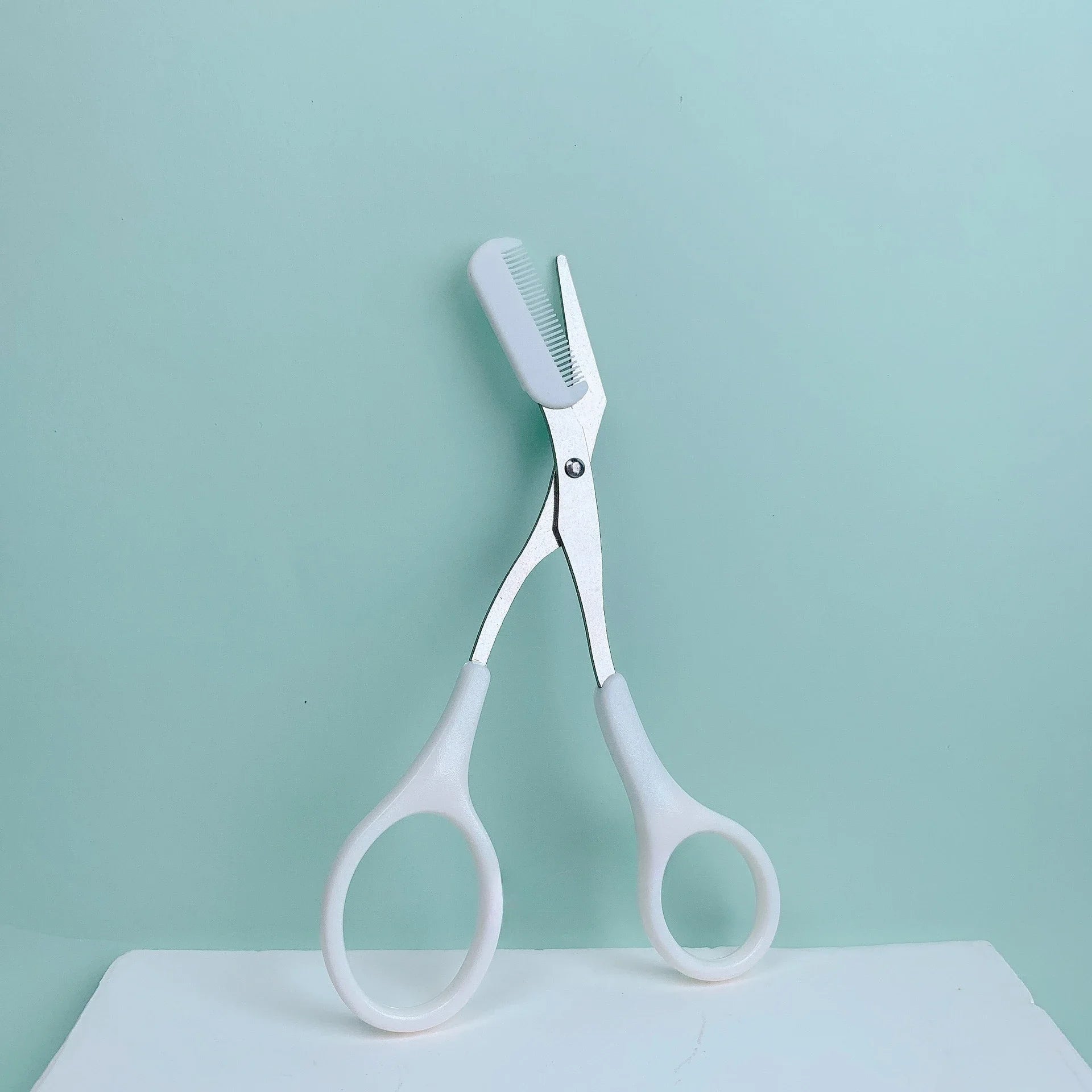 Pink stainless steel eyebrow trimming scissors with built-in comb for precise grooming and shaping of eyebrows.