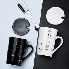 Two ceramic Pisces zodiac mugs with matching lids and spoons are displayed on a split background.