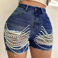High-waisted blue denim shorts featuring distressed holes embellished with draped pearl chains.