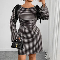 A person wears a black and white plaid long-sleeved dress with knot details on the shoulders.