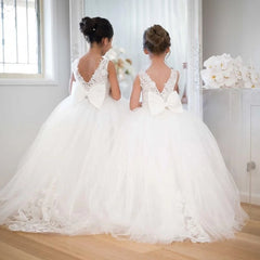Two girls stand side-by-side wearing floor-length white lace and tulle flower girl dresses.