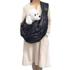 A person wears a black quilted sling carrier containing a small white plush dog.