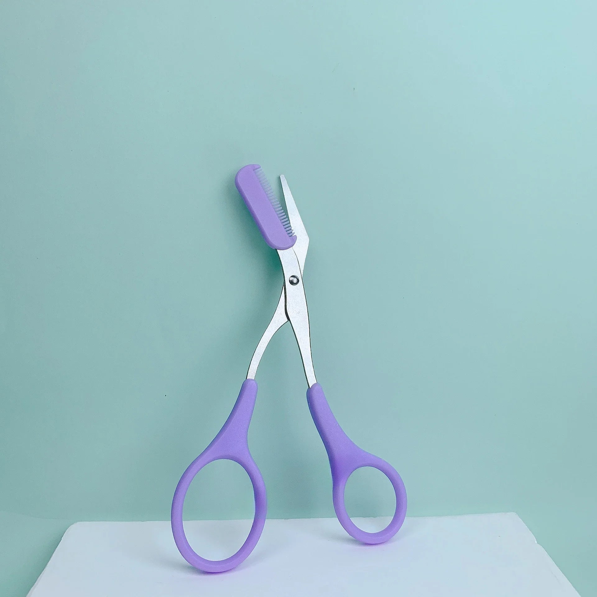 Pink stainless steel eyebrow trimming scissors with built-in comb for precise grooming and shaping of eyebrows.