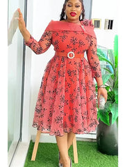 A woman wears a coral-colored, knee-length dress with a black floral print and a matching belt.