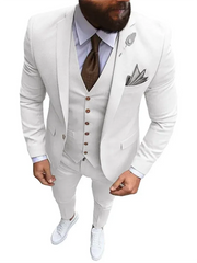 A man wears a white three-piece slim-fit suit with a brown tie and white sneakers.