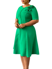 A woman wears a knee-length green A-line dress with short sleeves, button details, and floral trim.