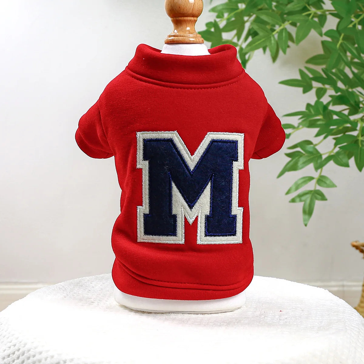 A red, long-sleeved dog hoodie featuring a large navy blue letter M patch on the back.