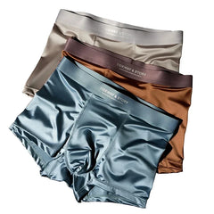 Three pairs of satin ice silk boxer shorts in blue, brown, and grey stacked on each other.