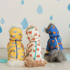 Three dogs wearing colorful, hooded, four-legged waterproof raincoats sit facing away from the camera.