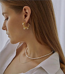 A woman wears a layered necklace featuring a strand of oval white pearls and a gold chain.