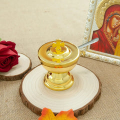 A golden communion cup with a cross on the lid and a matching spoon sits on a wooden base.