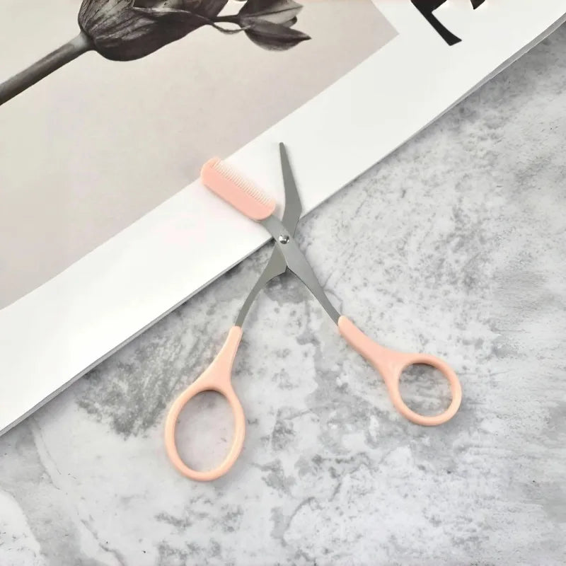 Pink stainless steel eyebrow trimming scissors with built-in comb for precise grooming and shaping of eyebrows.