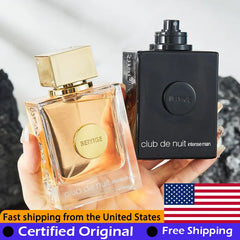 A hand holds two bottles of Armaf Club de Nuit Intense Man perfume against a dark background.