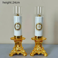 Two gold-toned Catholic oil lamp candlesticks with glass windshields and religious IHS symbols.