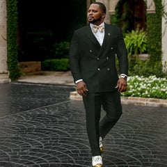 A man wears a dark green double-breasted suit with a white shirt and a gold bow tie.