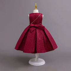 A sleeveless red formal dress for girls featuring a textured fabric, a large back bow, and a gold chain strap.