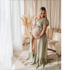 A pregnant woman wears a sage green, off-shoulder bohemian maxi dress with a front slit.
