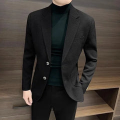 A man wears a black single-breasted blazer with a textured pattern over a black turtleneck.