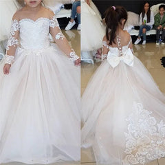 A girl wears a floor-length champagne ball gown with lace sleeves and a large back bow.