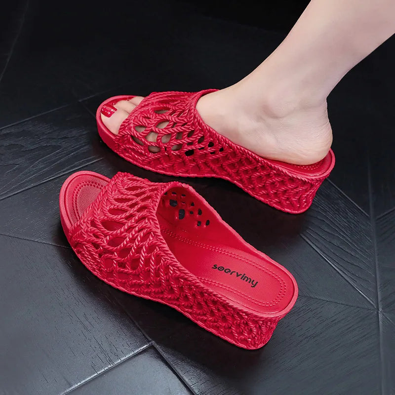 A pair of red wedge slippers with a hollow-out woven design and a thick platform sole.